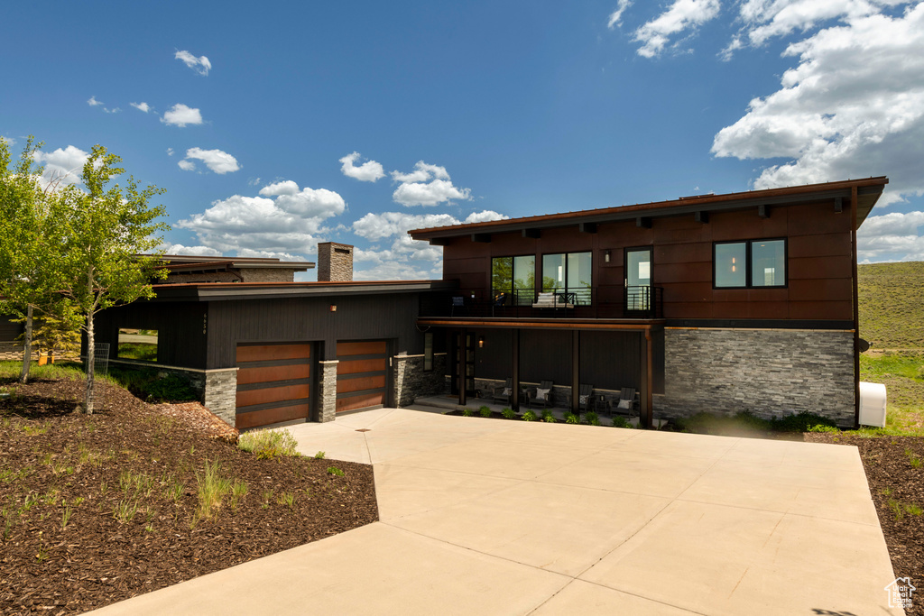 Contemporary house featuring stone siding, a balcony, and driveway
