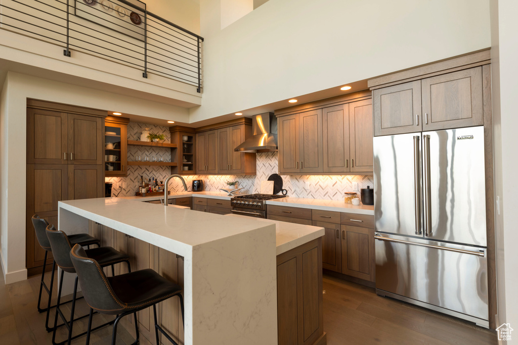 Kitchen featuring high end appliances, wall chimney exhaust hood, decorative backsplash, dark wood-style floors, and a sink