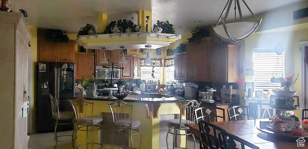 Kitchen featuring black refrigerator with ice dispenser, dark countertops, stainless steel microwave, and a kitchen bar