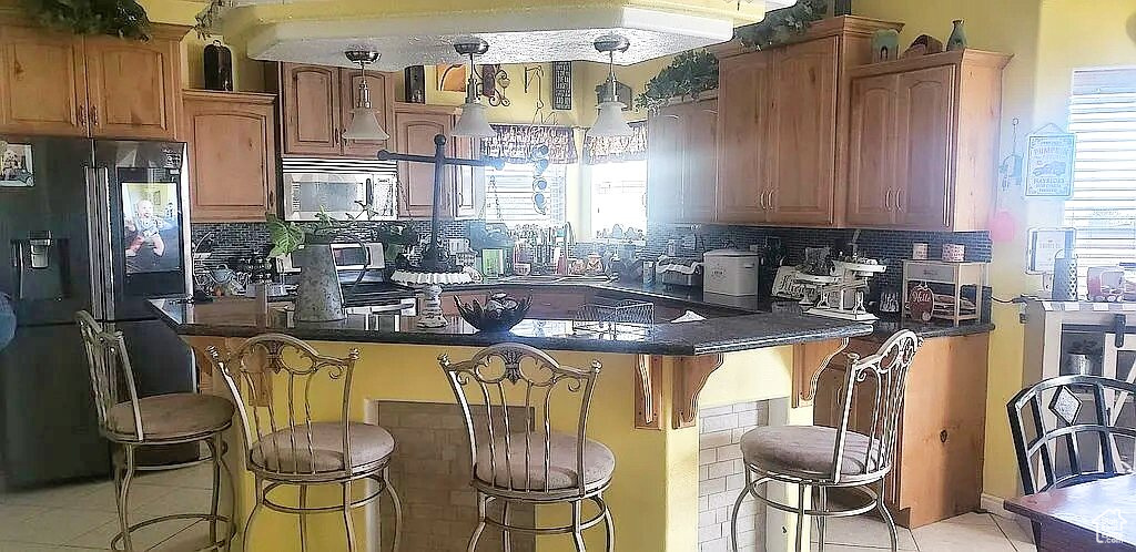 Kitchen with stainless steel microwave, black fridge, a breakfast bar, and decorative backsplash