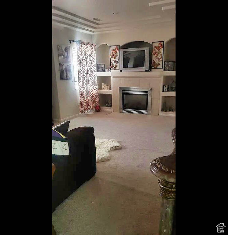 Carpeted living area with a tiled fireplace and ornamental molding