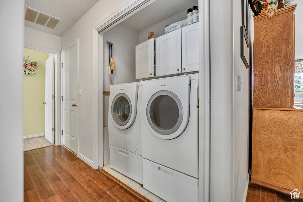Laundry room with separate washer and dryer, cabinet space, dark wood-type flooring, and baseboards