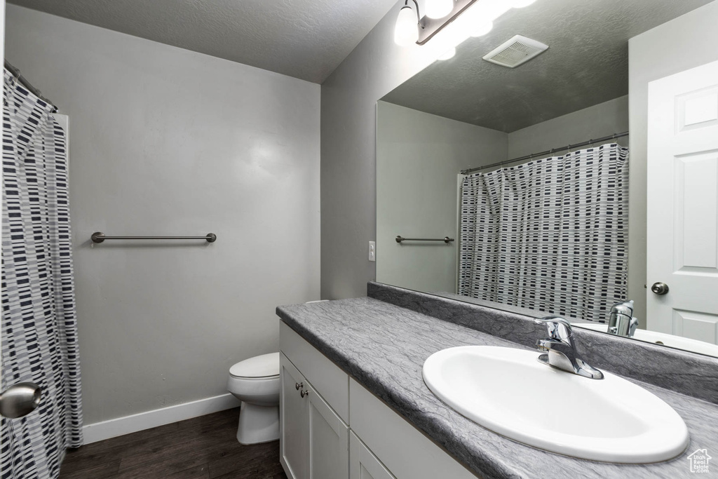 Full bathroom with toilet, wood finished floors, vanity, baseboards, and a heating unit
