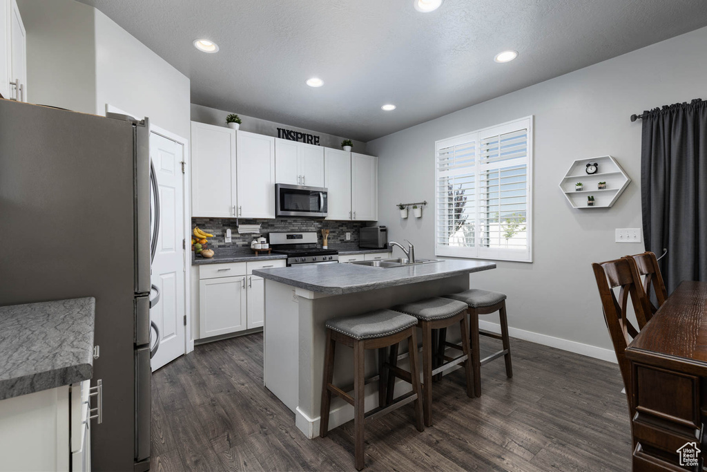 Kitchen featuring stainless steel appliances, dark wood finished floors, a breakfast bar, a sink, and baseboards