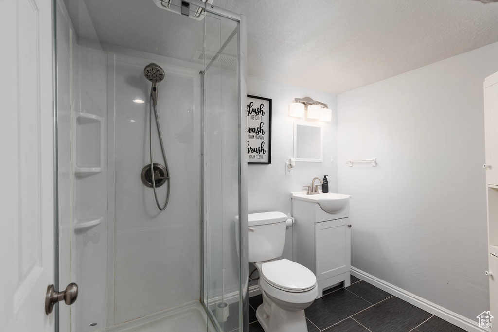 Bathroom featuring a stall shower, vanity, toilet, baseboards, and tile patterned floors