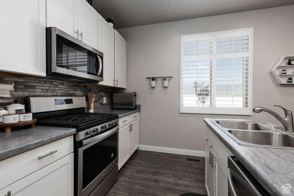 Kitchen featuring appliances with stainless steel finishes, a sink, decorative backsplash, dark wood finished floors, and baseboards