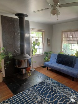 Living room featuring a wood stove, ceiling fan, wood finished floors, and baseboards