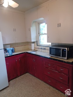 Kitchen with stainless steel microwave, freestanding refrigerator, decorative backsplash, arched walkways, and ceiling fan