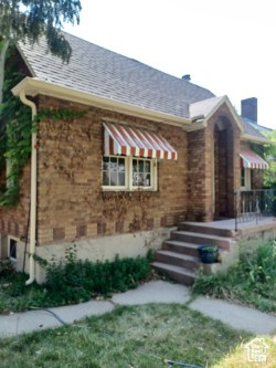 View of front facade featuring brick siding, roof with shingles, and a chimney