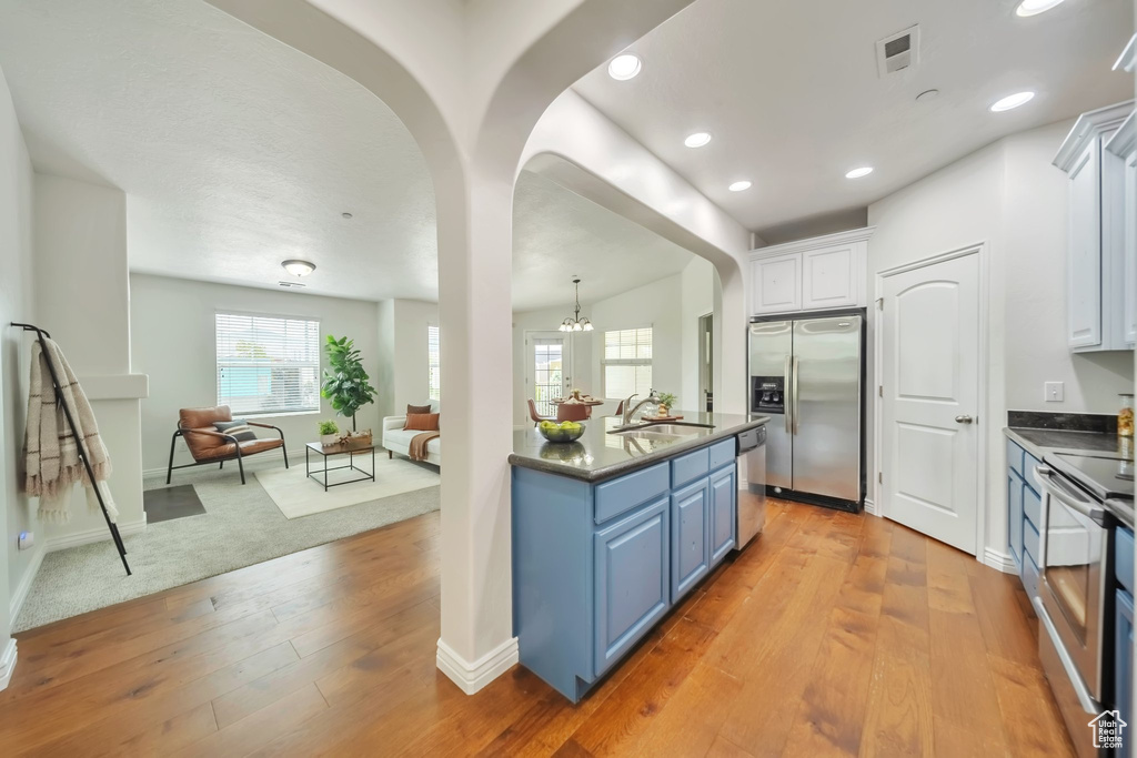 Kitchen featuring stainless steel appliances, blue cabinetry, dark countertops, open floor plan, and white cabinets