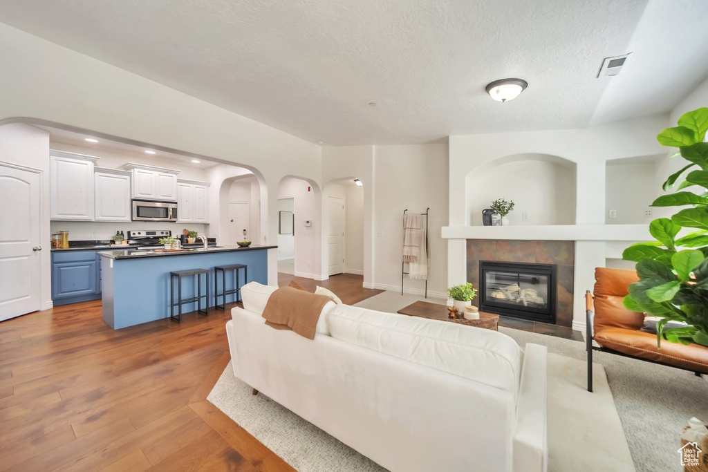 Living room featuring a tile fireplace, light wood-type flooring, arched walkways, recessed lighting, and a textured ceiling