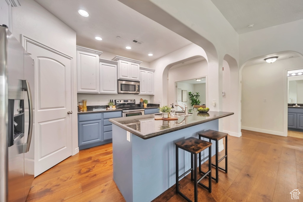 Kitchen featuring appliances with stainless steel finishes, arched walkways, a kitchen bar, light wood-style flooring, and recessed lighting