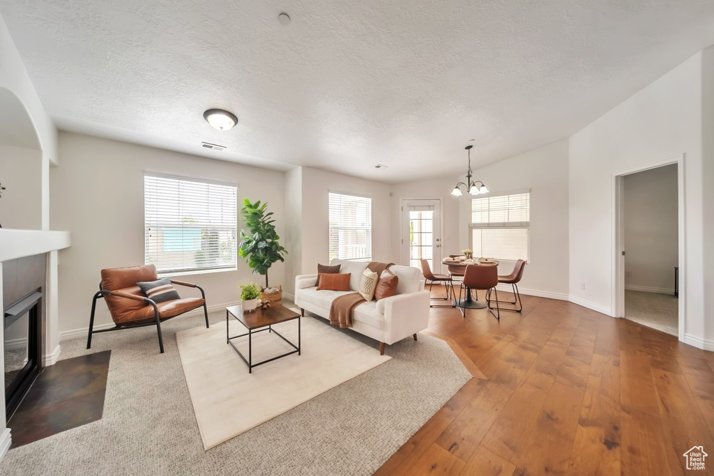 Living room featuring a fireplace with flush hearth, a chandelier, baseboards, wood finished floors, and a textured ceiling