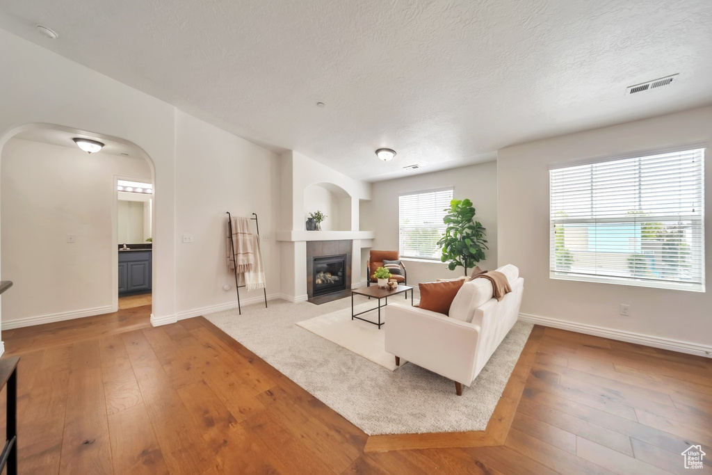 Living area featuring hardwood / wood-style flooring, a tile fireplace, arched walkways, baseboards, and a textured ceiling