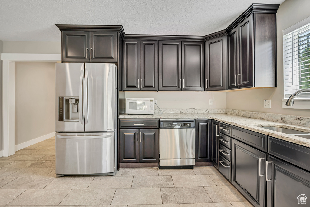 Kitchen with appliances with stainless steel finishes, a sink, light stone countertops, a textured ceiling, and baseboards