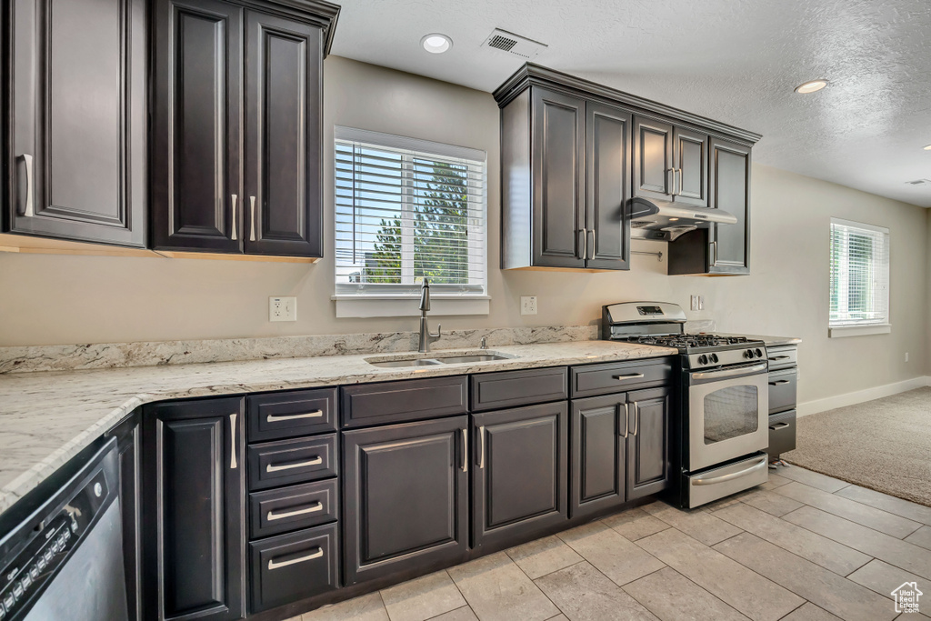 Kitchen featuring appliances with stainless steel finishes, a sink, under cabinet range hood, light stone countertops, and baseboards
