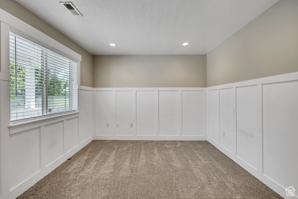 Carpeted spare room featuring a decorative wall, a textured ceiling, wainscoting, and recessed lighting