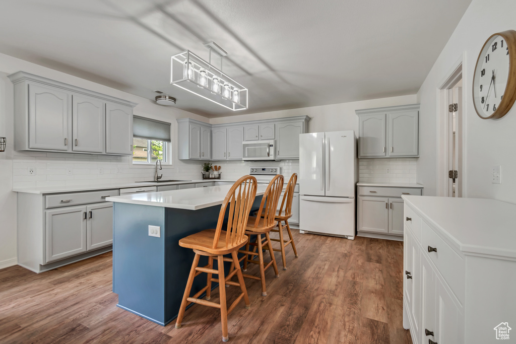 Kitchen featuring white appliances, gray cabinetry, decorative backsplash, a breakfast bar area, and dark wood finished floors