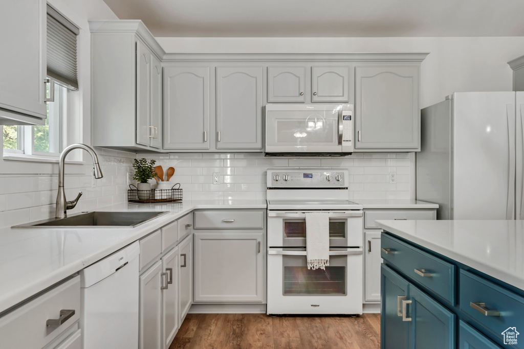 Kitchen featuring white appliances, a sink, blue cabinets, light countertops, and backsplash