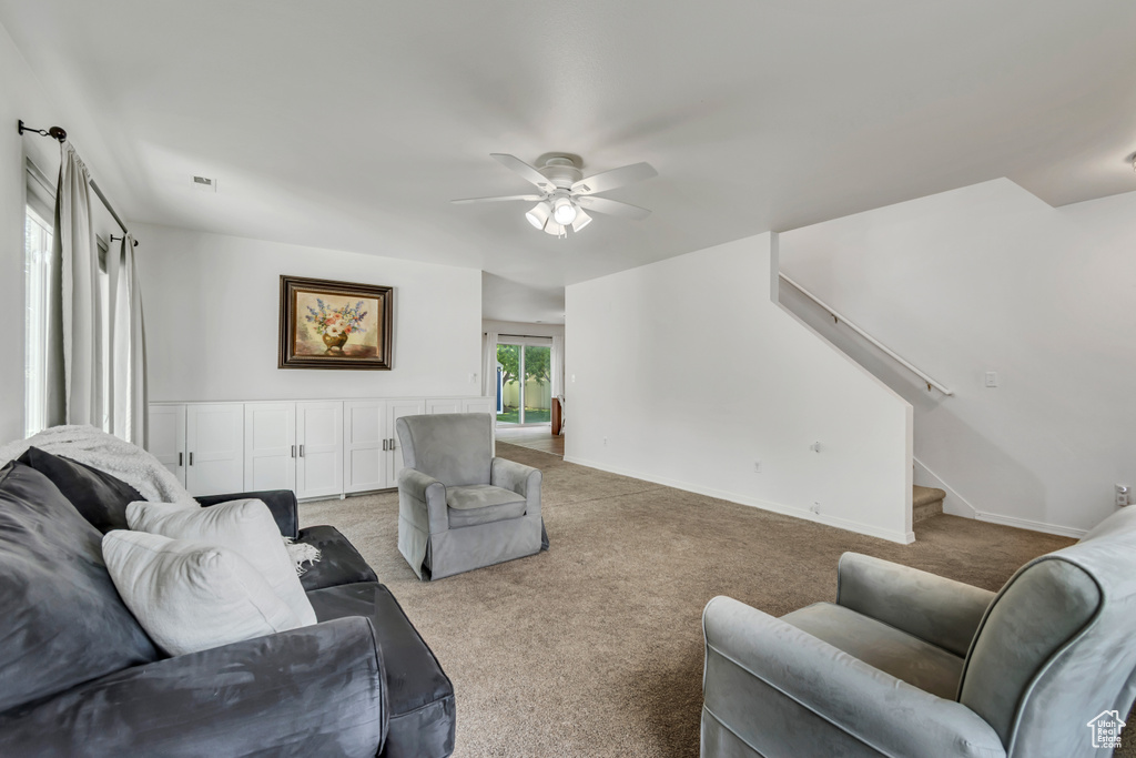 Living area with light carpet, ceiling fan, stairs, and baseboards