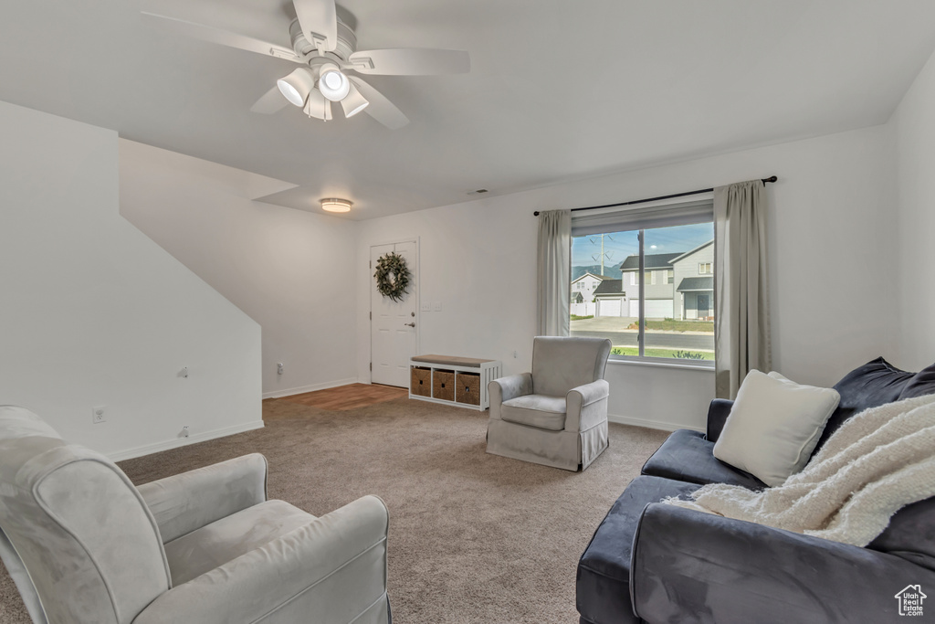 Carpeted living room with a ceiling fan and baseboards