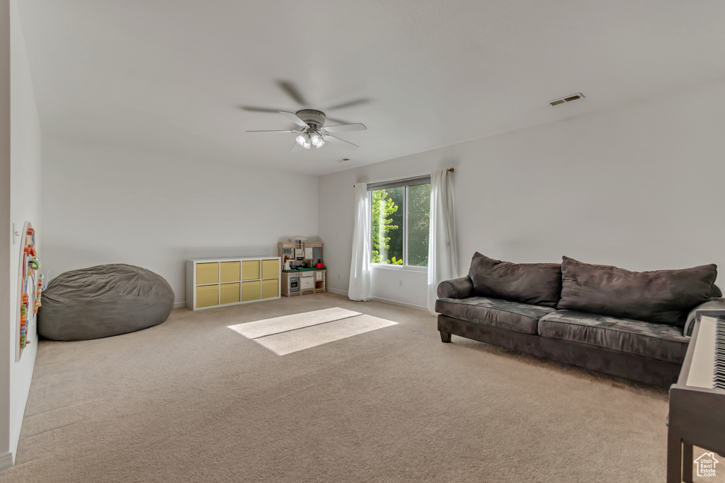 Carpeted living area featuring ceiling fan and baseboards