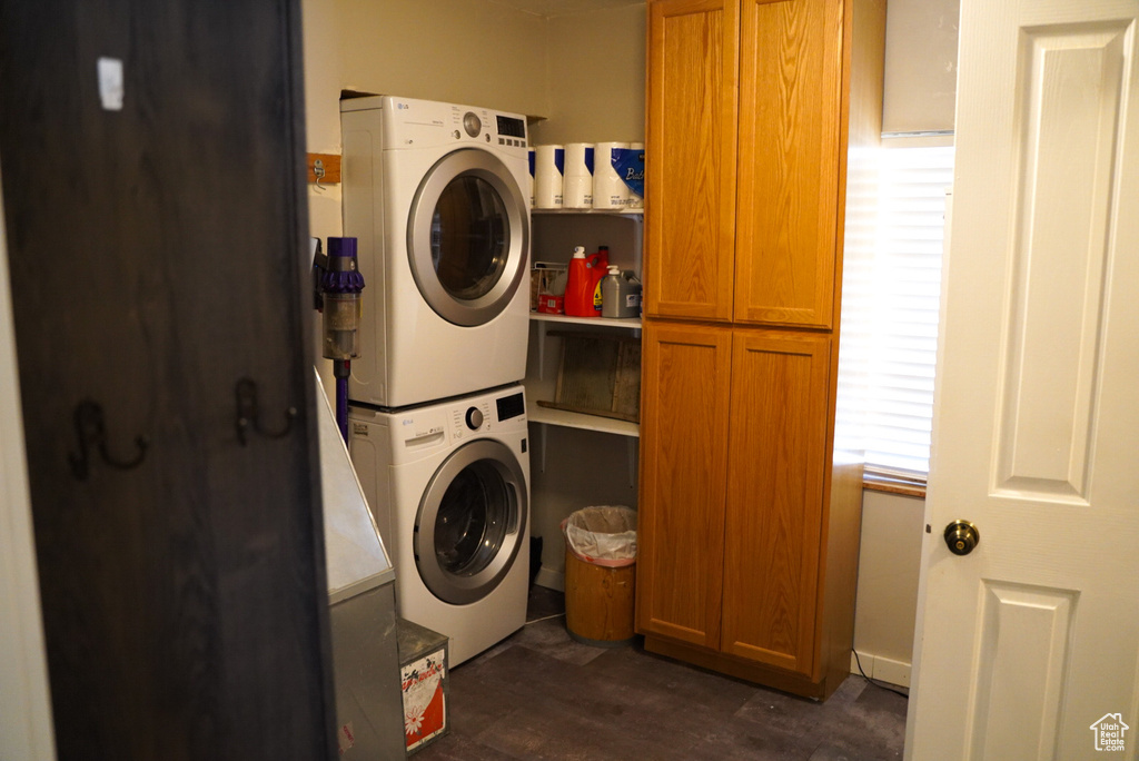 Laundry room with cabinet space, stacked washer / dryer, and dark wood-style flooring