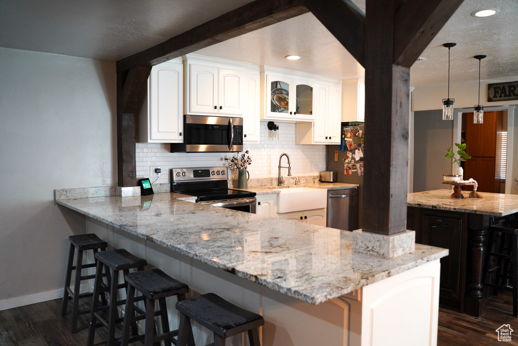 Kitchen with appliances with stainless steel finishes, backsplash, light stone counters, a kitchen bar, and white cabinetry