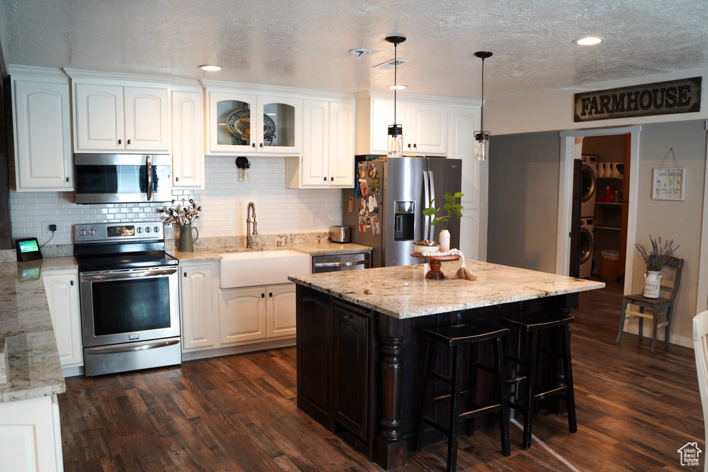 Kitchen featuring appliances with stainless steel finishes, a sink, white cabinetry, decorative backsplash, and a textured ceiling