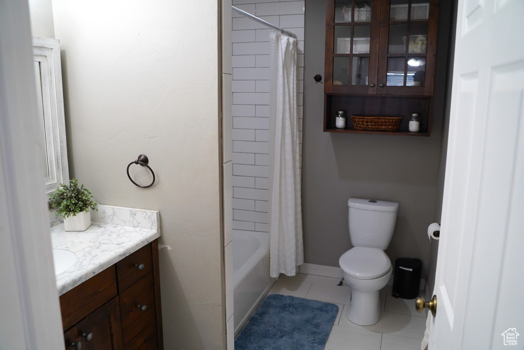 Full bathroom with toilet, tile patterned floors, vanity, shower / bath combo with shower curtain, and baseboards