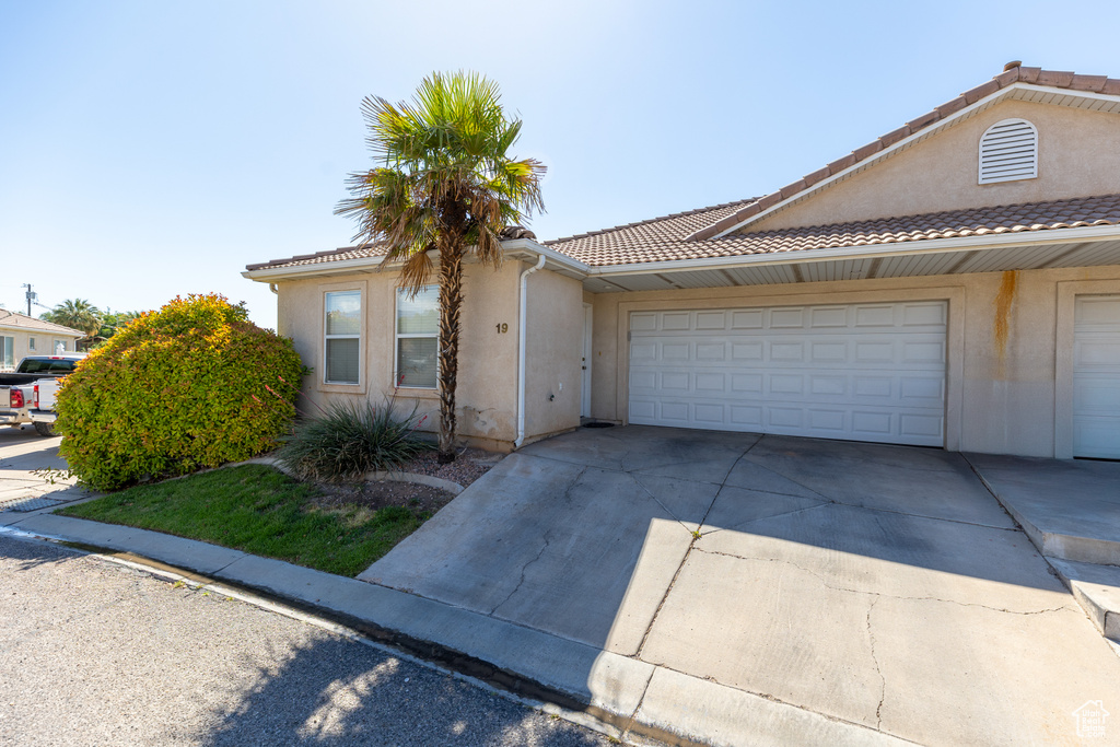View of front of property with driveway, stucco siding, a tile roof, and a garage