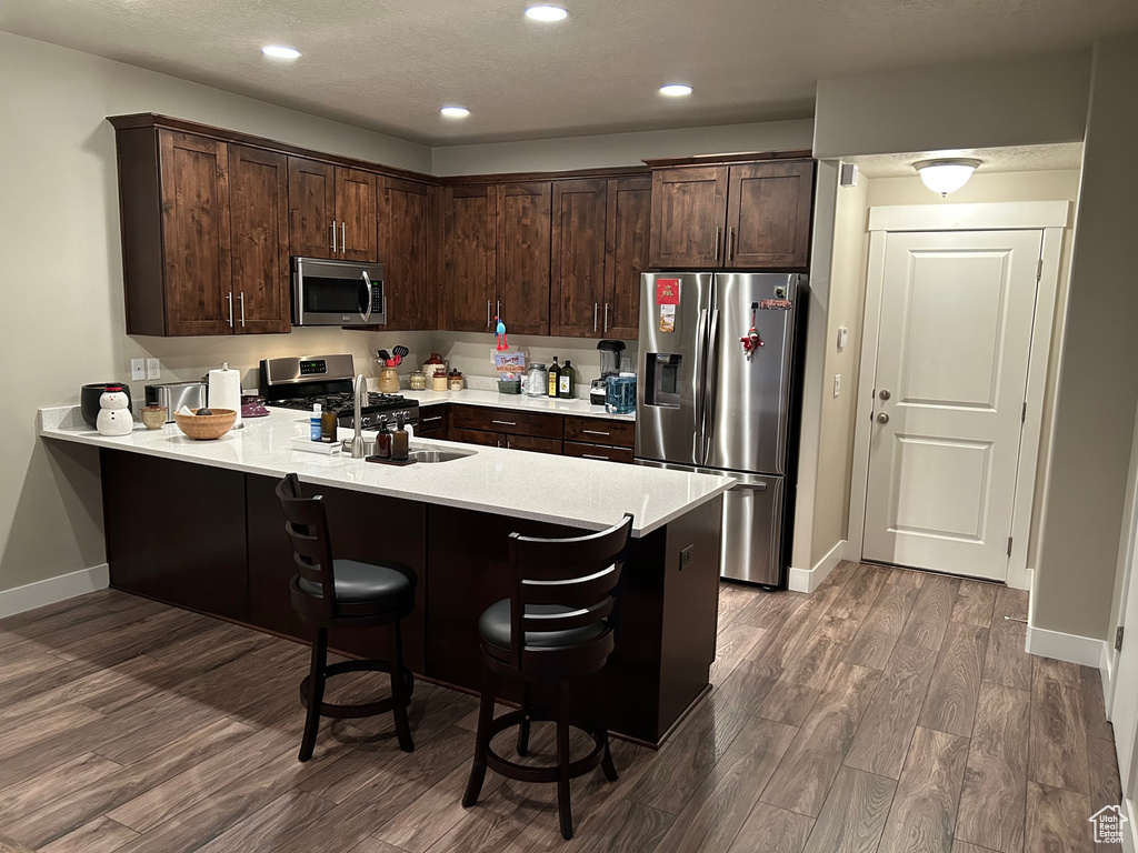 Kitchen with stainless steel appliances, dark brown cabinets, dark wood-type flooring, a peninsula, and light countertops