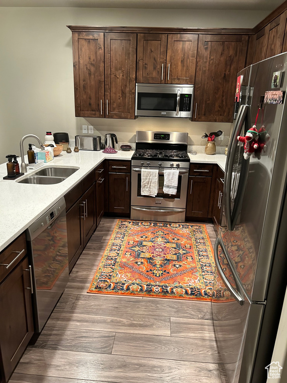 Kitchen with stainless steel appliances, a sink, wood finished floors, dark brown cabinets, and light countertops