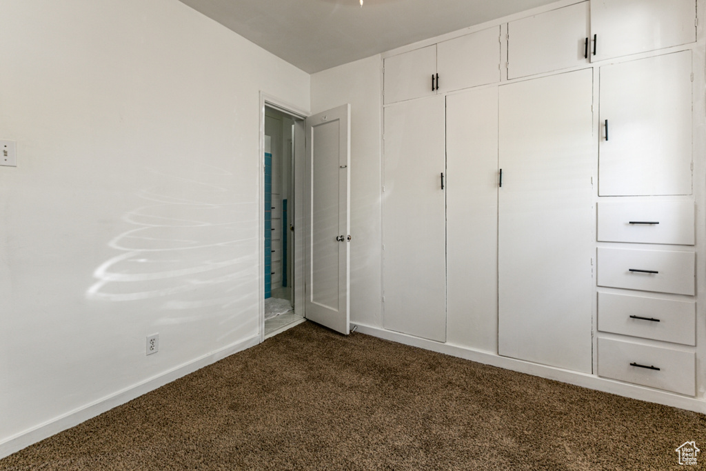 Unfurnished bedroom featuring dark colored carpet, baseboards, and a closet