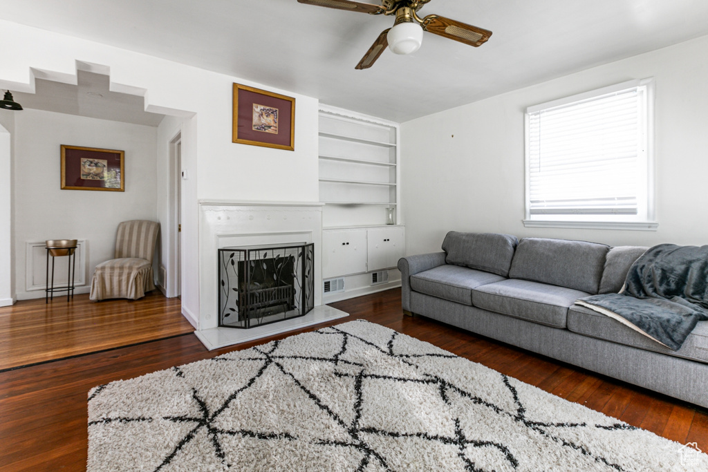 Living room with a fireplace, built in features, a ceiling fan, and wood finished floors