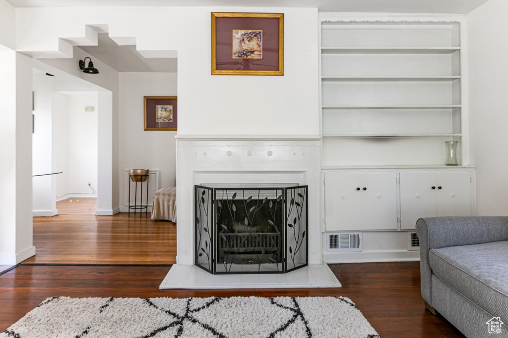 Living area with dark wood-style flooring, a fireplace with raised hearth, built in features, and baseboards