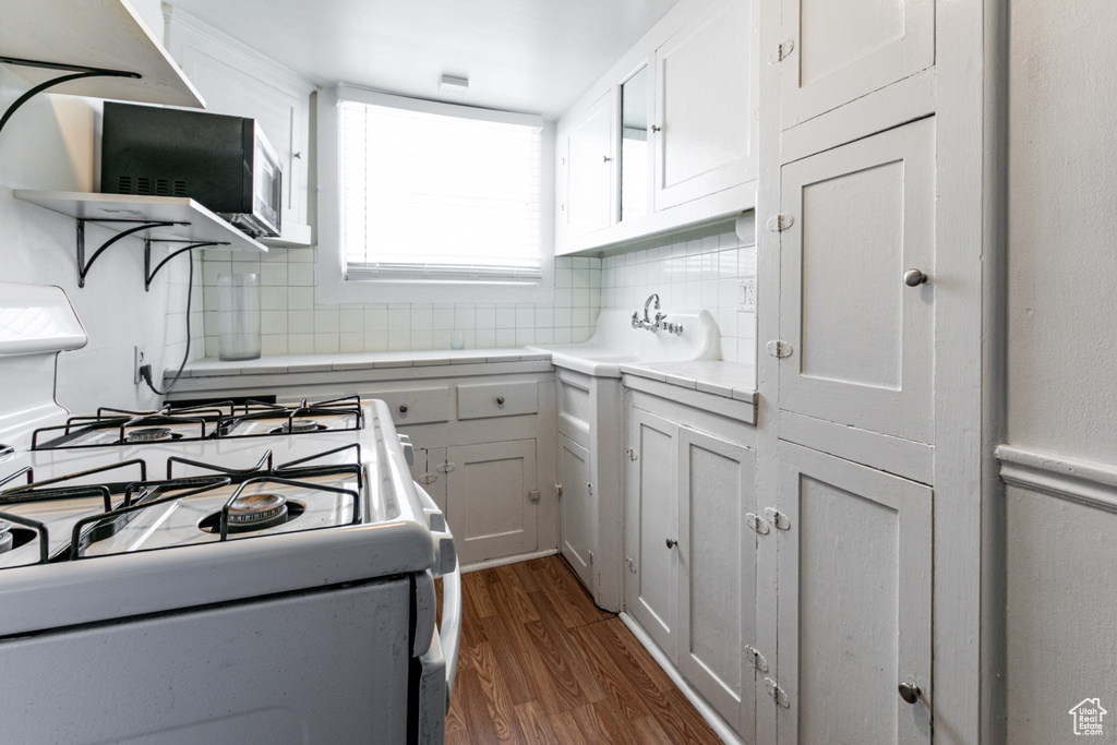 Kitchen featuring white gas stove, stainless steel microwave, decorative backsplash, dark wood-style floors, and a sink