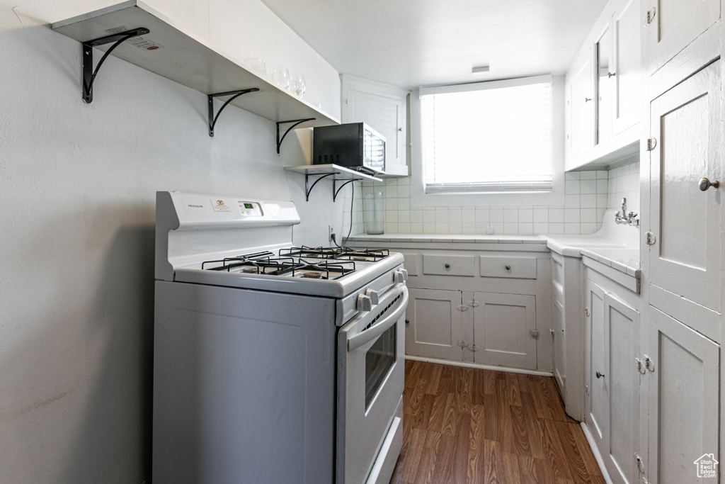 Kitchen featuring white range with gas stovetop, open shelves, dark wood-style floors, backsplash, and light countertops