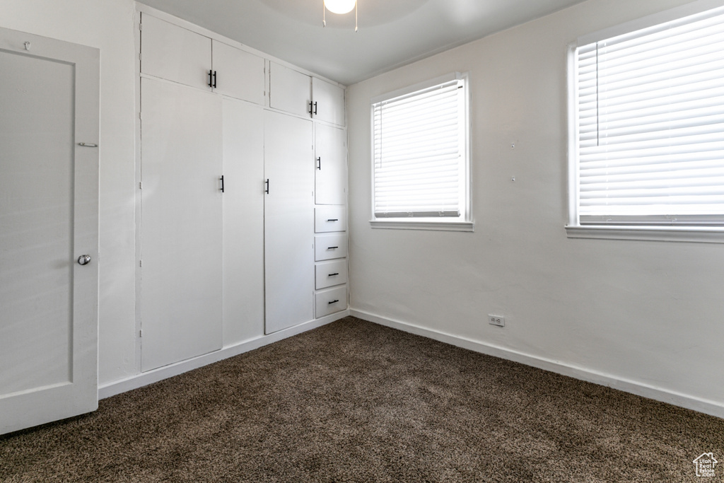 Unfurnished bedroom with dark carpet, multiple windows, a closet, and baseboards