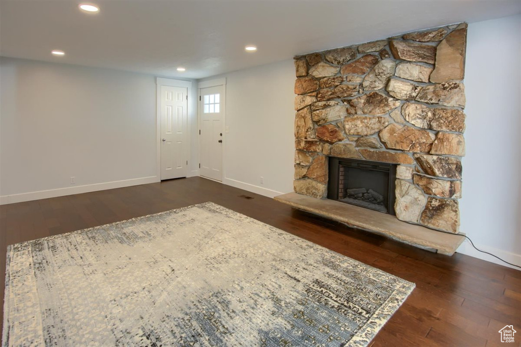 Unfurnished living room with dark wood-style flooring, baseboards, a stone fireplace, and recessed lighting