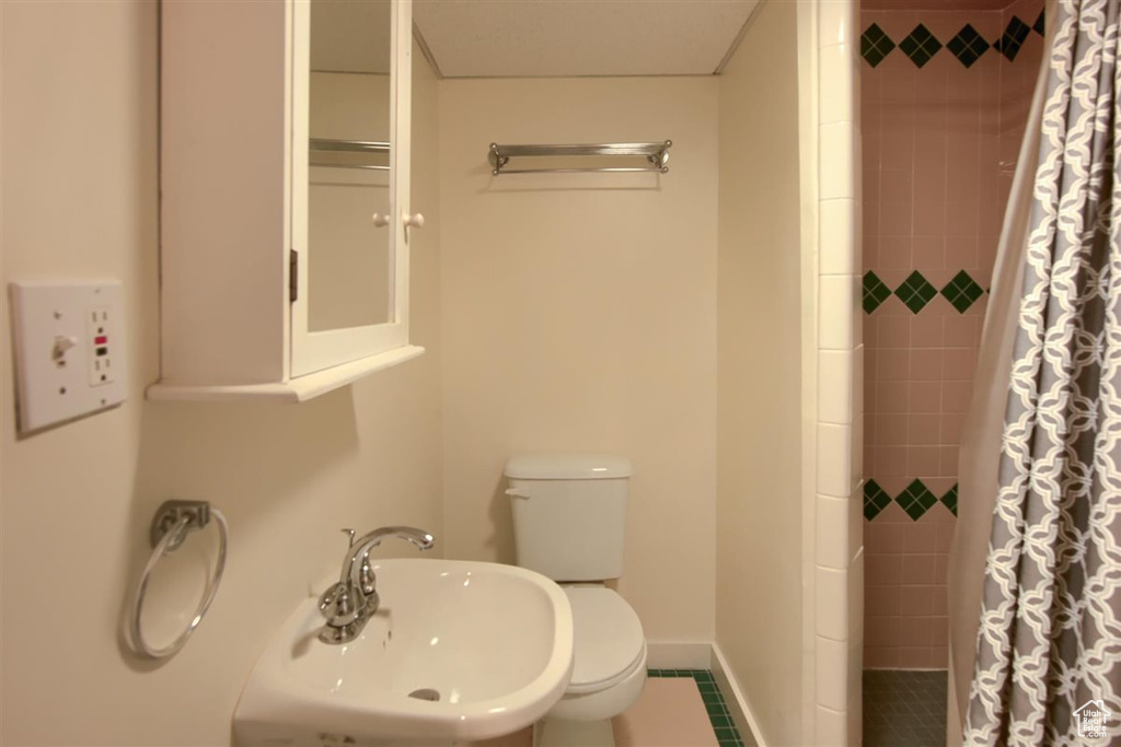 Full bath featuring a sink, tiled shower, toilet, and baseboards