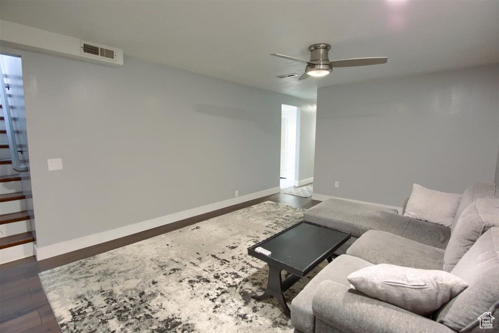 Living room featuring a ceiling fan, dark wood-type flooring, baseboards, and stairway