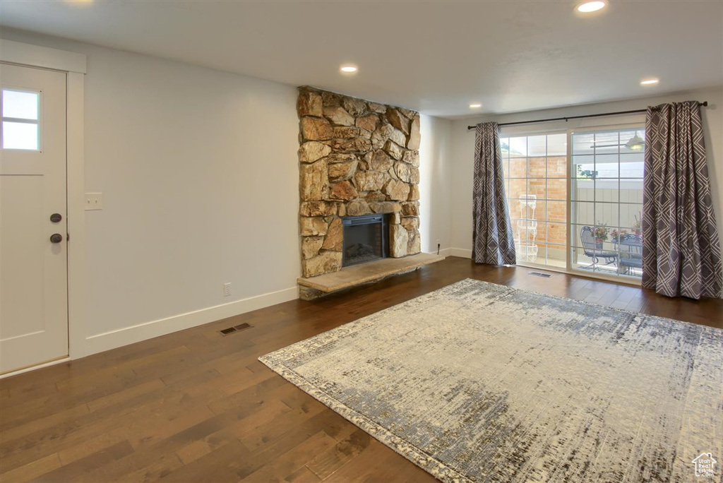 Unfurnished living room featuring baseboards, dark wood-style floors, a stone fireplace, and recessed lighting