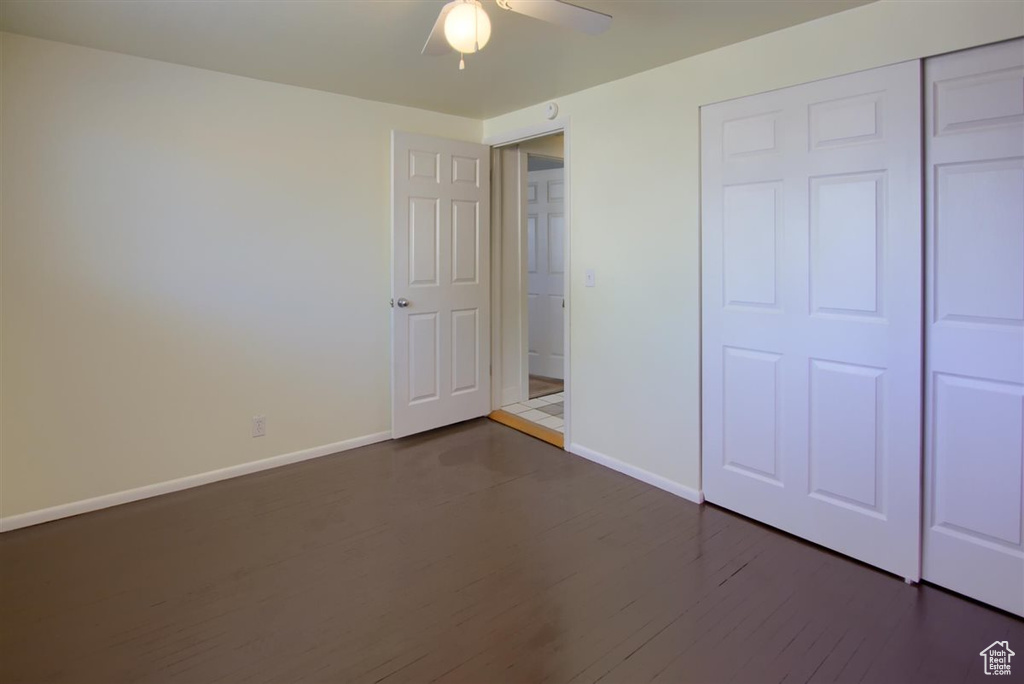 Unfurnished bedroom featuring baseboards, a closet, a ceiling fan, and dark wood finished floors