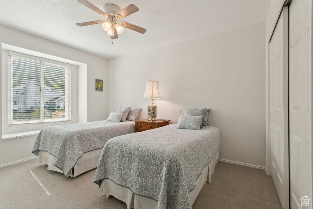 Bedroom with a closet, baseboards, light colored carpet, and ceiling fan