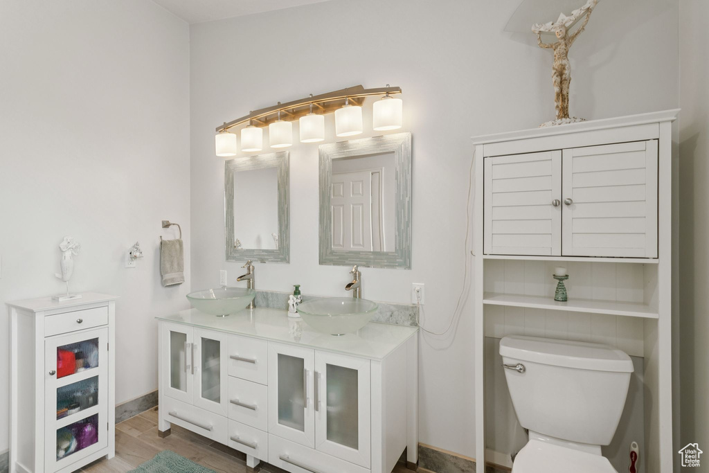 Full bathroom with double vanity, toilet, and wood finished floors