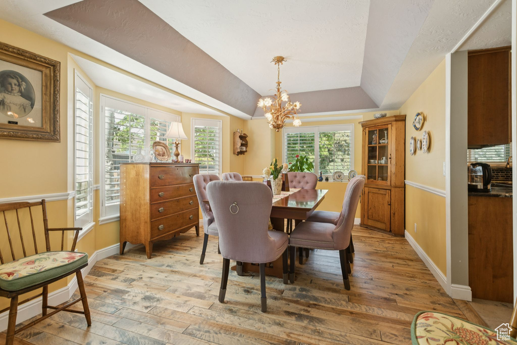 Dining room featuring light wood-type flooring, a chandelier, a raised ceiling, and baseboards