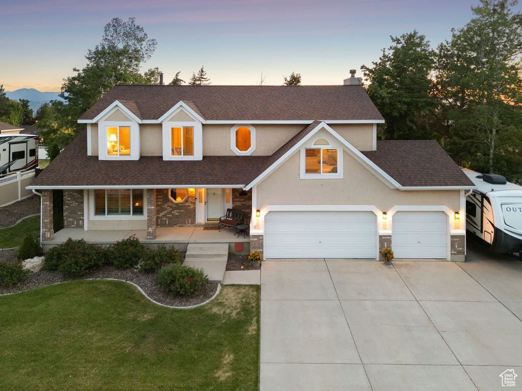 Traditional home with stone siding, roof with shingles, driveway, a front lawn, and covered porch