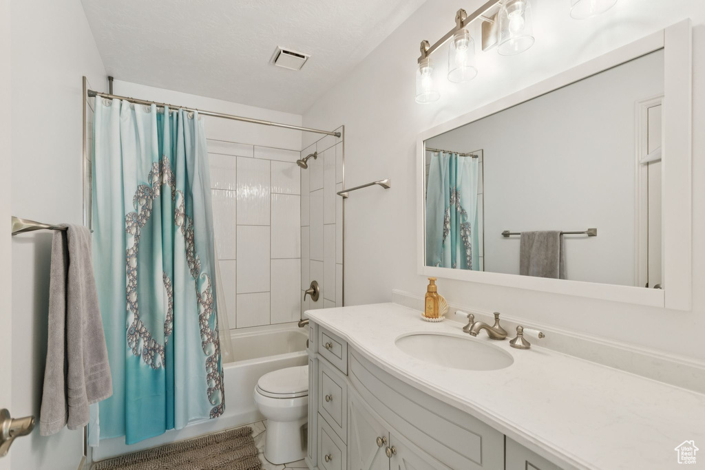 Bathroom featuring vanity, shower / bathtub combination with curtain, and toilet