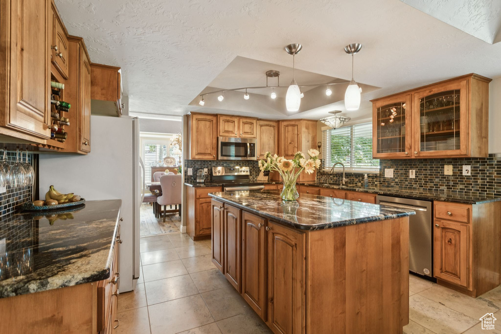 Kitchen featuring stainless steel appliances, backsplash, brown cabinetry, glass insert cabinets, and a textured ceiling